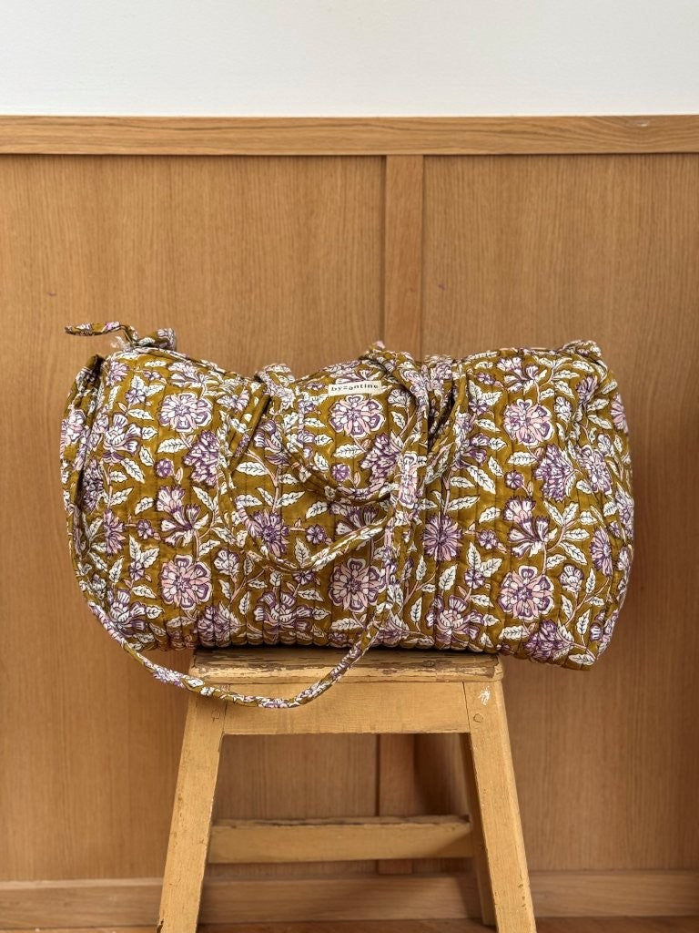 Sac weekend matelassé Carthage Kaki de Byzantine, fleurs lilas sur fond kaki, posé sur un tabouret en bois