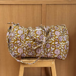 Sac weekend matelassé Carthage Kaki de Byzantine, fleurs lilas sur fond kaki, posé sur un tabouret en bois