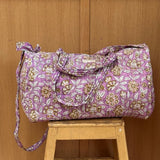 Sac weekend matelassé Carthage Lilas de Byzantine, imprimé fleuri lilas, posé sur un tabouret en bois