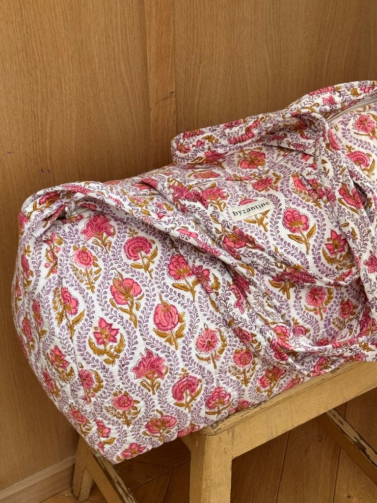 Sac weekend Éphèse Rose posé sur un tabouret, fleurs rose corail et feuillages lilas