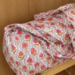Sac weekend Éphèse Rose posé sur un tabouret, fleurs rose corail et feuillages lilas