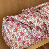 Sac weekend Éphèse Rose posé sur un tabouret, fleurs rose corail et feuillages lilas