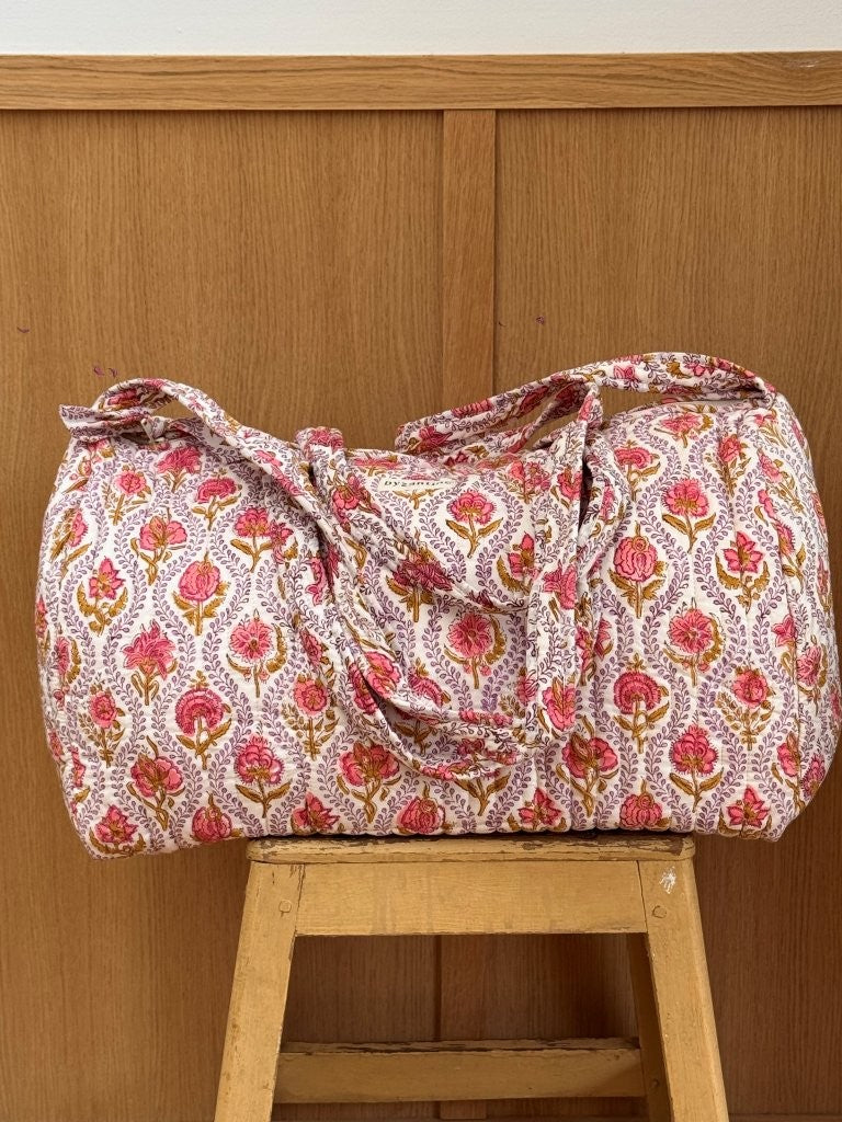 Sac weekend matelassé Éphèse Rose de Byzantine, imprimé fleuri rose, posé sur un tabouret en bois
