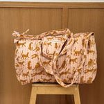 Sac weekend matelassé Fauve Rose de Byzantine, guépards ocre sur fond rose pâle, posé sur un tabouret en bois