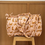 Sac weekend matelassé Fauve Rose de Byzantine, guépards ocre sur fond rose pâle, posé sur un tabouret en bois