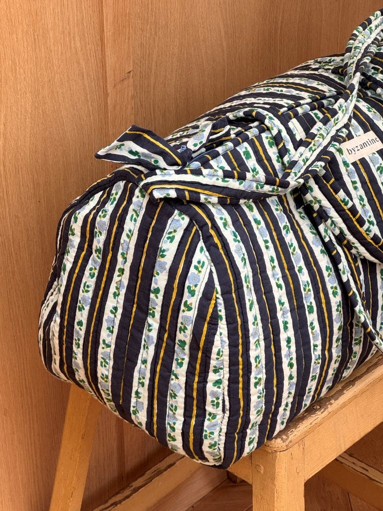 Sac weekend Flora Bleu marine sur un tabouret, rayures bleu marine et guirlandes de fleurs