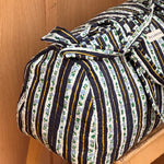 Sac weekend Flora Bleu marine sur un tabouret, rayures bleu marine et guirlandes de fleurs