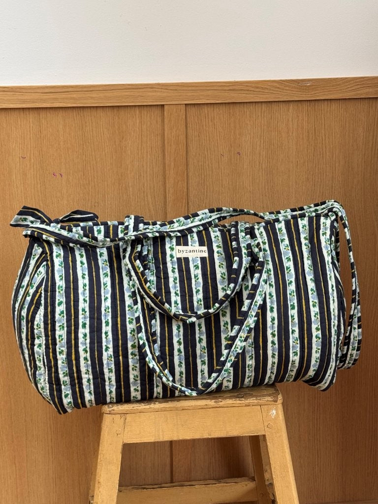 Sac weekend matelassé Flora Bleu marine de Byzantine, rayures fleuries bleu marine, posé sur un tabouret en bois