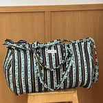 Sac weekend matelassé Flora Bleu marine de Byzantine, rayures fleuries bleu marine, posé sur un tabouret en bois