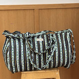 Sac weekend matelassé Flora Bleu marine de Byzantine, rayures fleuries bleu marine, posé sur un tabouret en bois