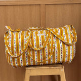 Sac weekend matelassé Flora Passion de Byzantine, rayures fleuries jaune moutarde, posé sur un tabouret en bois