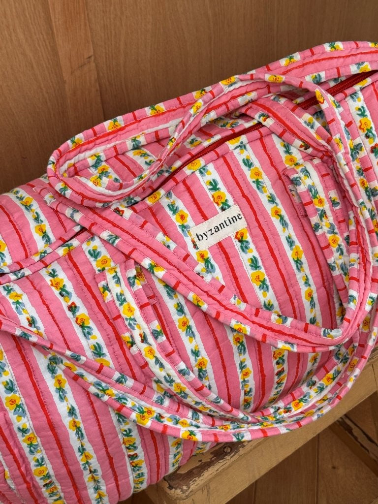 Gros plan sur le sac weekend Flora Rose, anses et étiquette Byzantine, rayures roses fleuries