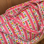 Gros plan sur le sac weekend Flora Rose, anses et étiquette Byzantine, rayures roses fleuries