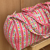 Sac weekend Flora Rose sur un tabouret, rayures roses et guirlandes de petites fleurs jaunes