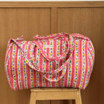 Sac weekend matelassé Flora Rose de Byzantine, rayures roses fleuries, posé sur un tabouret en bois