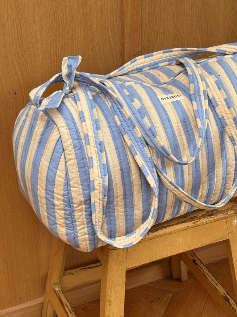 Sac weekend Pacha Bleu ciel posé sur un tabouret, larges rayures bleu ciel et écru