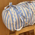 Sac weekend Pacha Bleu ciel posé sur un tabouret, larges rayures bleu ciel et écru