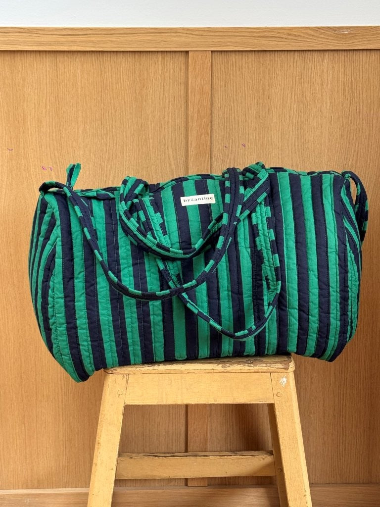Sac weekend matelassé Pacha Menthe de Byzantine, rayures vert menthe et bleu nuit, posé sur un tabouret en bois