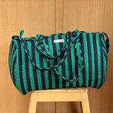 Sac weekend matelassé Pacha Menthe de Byzantine, rayures vert menthe et bleu nuit, posé sur un tabouret en bois