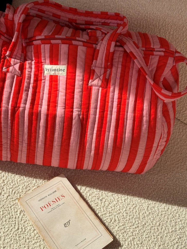 Sac weekend Pacha Tomato posé sur un canapé, un livre à côté, coton matelassé rayé