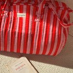 Sac weekend Pacha Tomato posé sur un canapé, un livre à côté, coton matelassé rayé