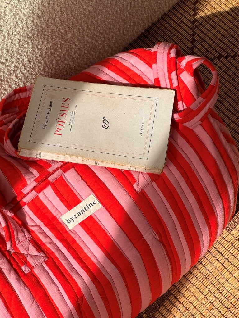 Sac weekend Pacha Tomato avec un livre de poésie posé dessus, rayures rouges et roses