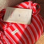 Sac weekend Pacha Tomato avec un livre de poésie posé dessus, rayures rouges et roses