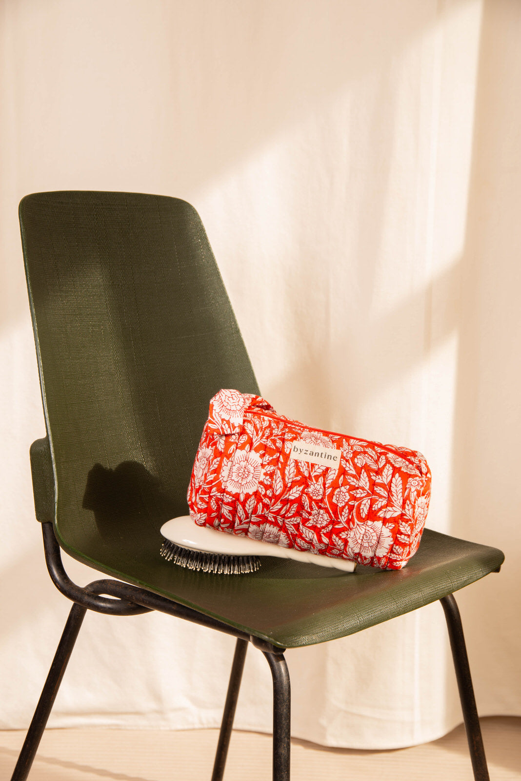 Trousse à crayons Antioche Tomato posée sur une assiette, sur une chaise verte