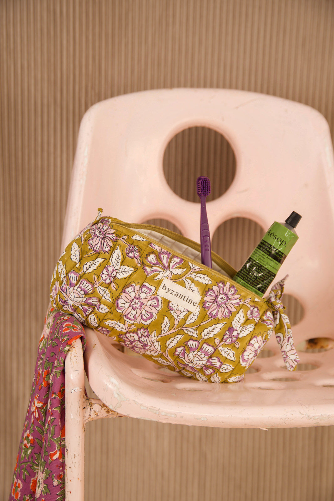 Trousse à crayons Carthage Kaki ouverte avec brosse à dents et tube, sur une chaise rose
