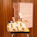 Trousse à crayons Fauve Rose avec pinceaux, sur un tabouret devant une caisse rose