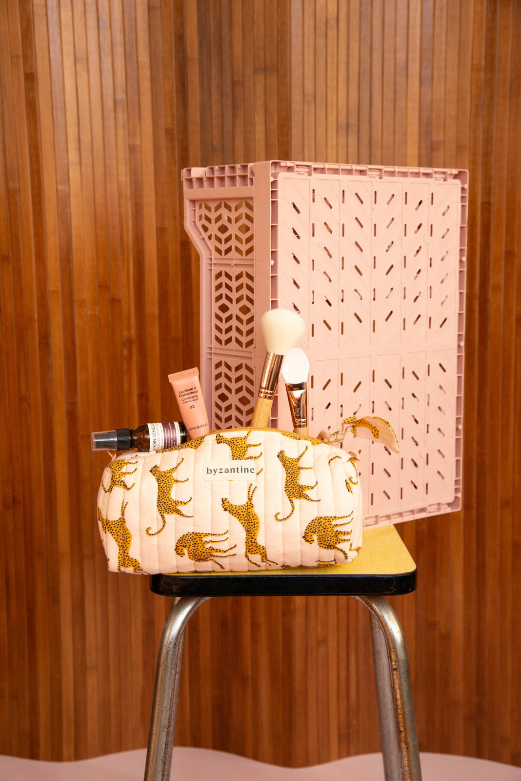 Trousse à crayons Fauve Rose avec pinceaux, sur un tabouret devant une caisse rose
