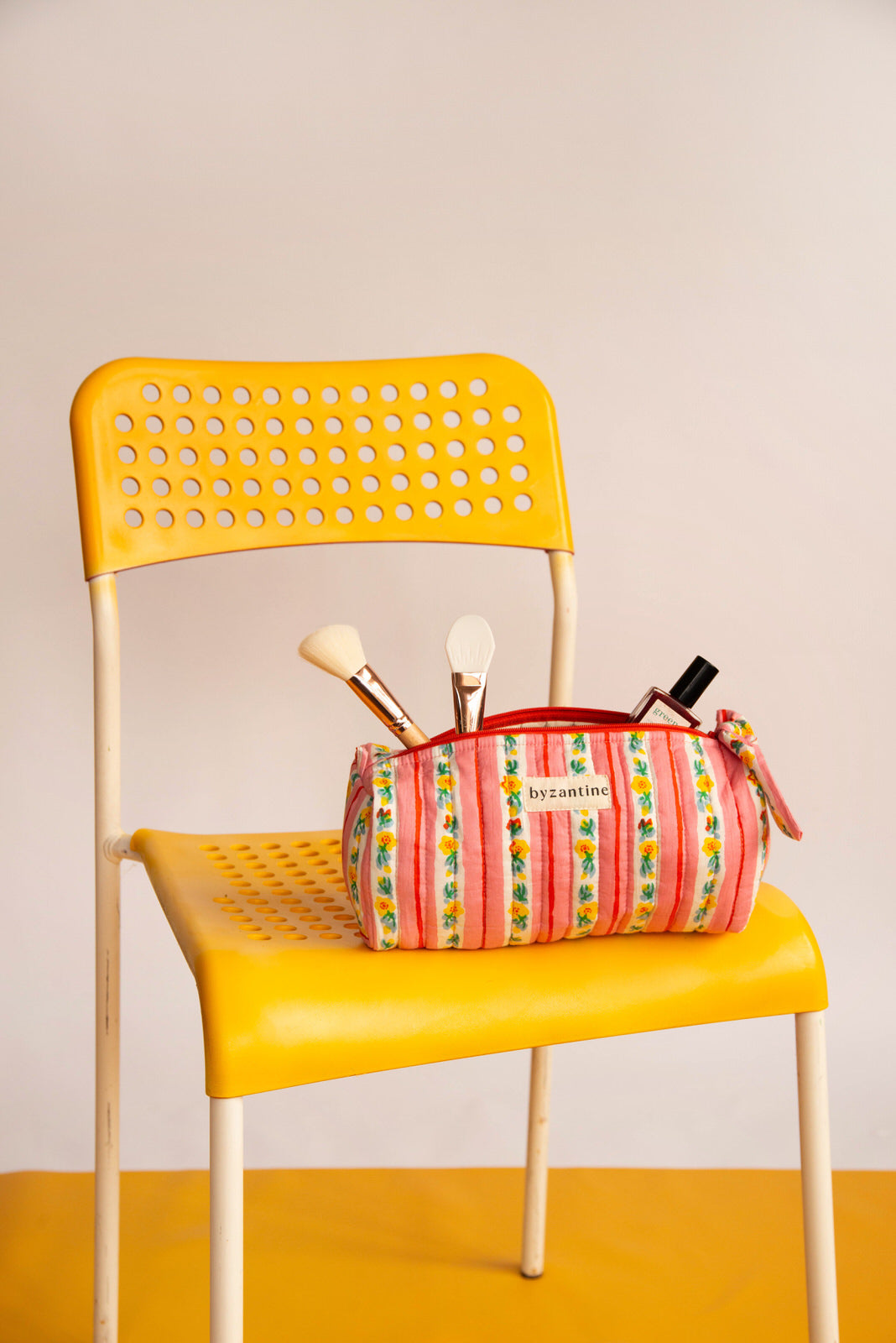 Trousse à crayons Flora Rose avec pinceaux de maquillage, posée sur une chaise jaune
