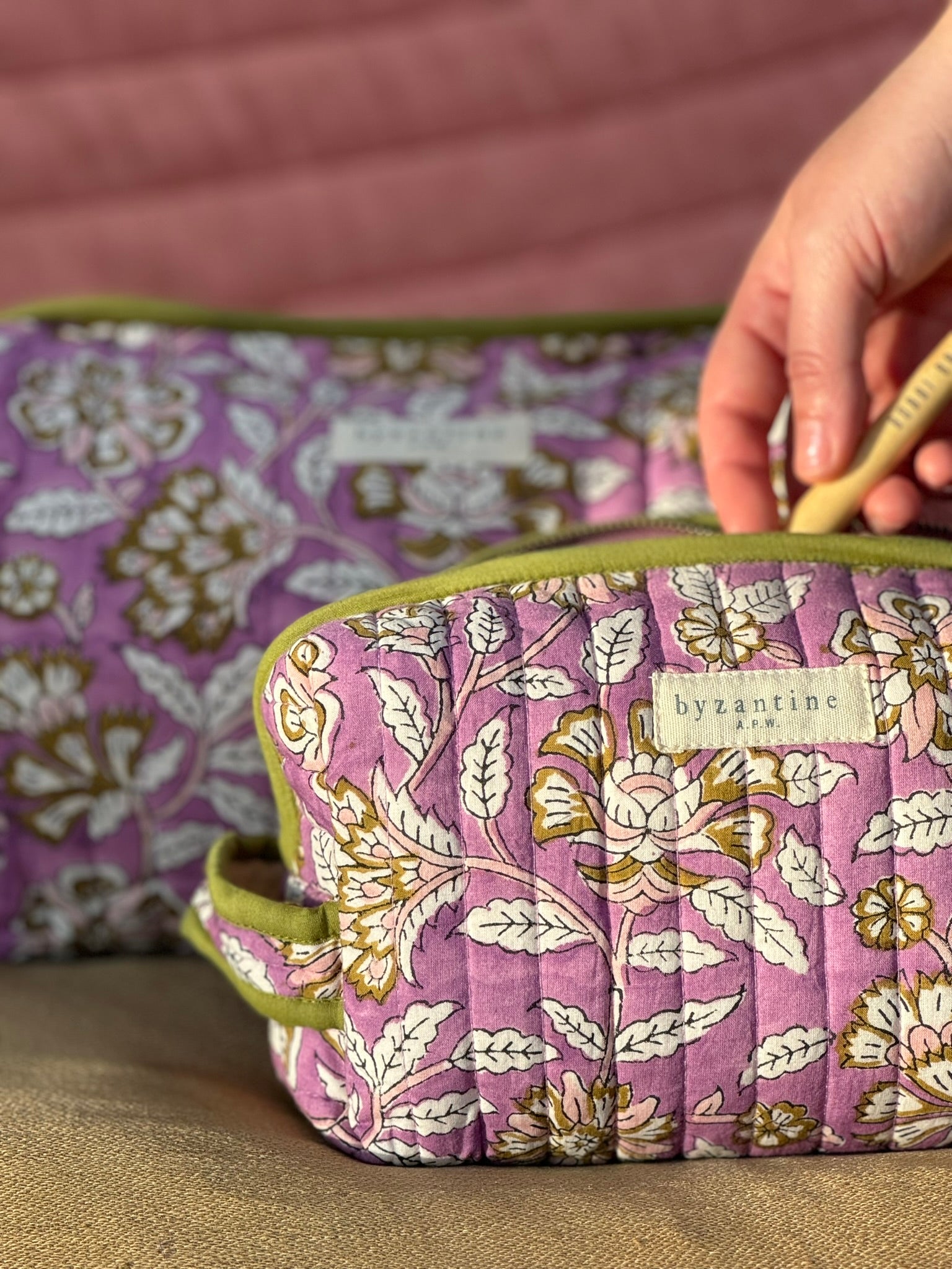 Main glissant une brosse à dents dans la petite trousse Carthage Lilas, devant la trousse de toilette XL
