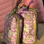 Main tenant la trousse de toilette XL Carthage Lilas par sa poignée, posée debout près de la petite trousse