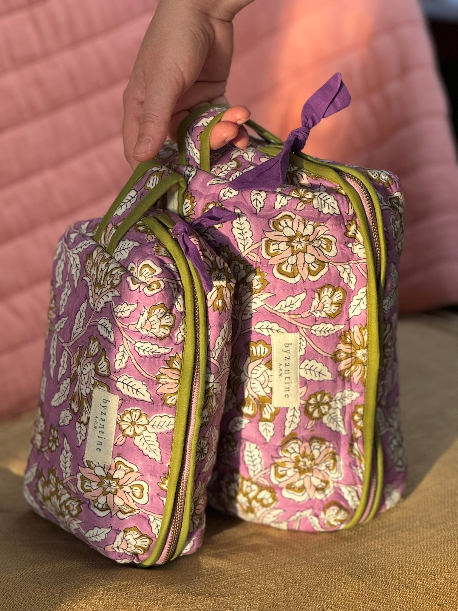 Main tenant la trousse de toilette XL Carthage Lilas par sa poignée, posée debout près de la petite trousse