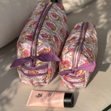 Grande et petite trousses Éphèse Rose debout sur un canapé, nœuds lilas, tube de crème devant