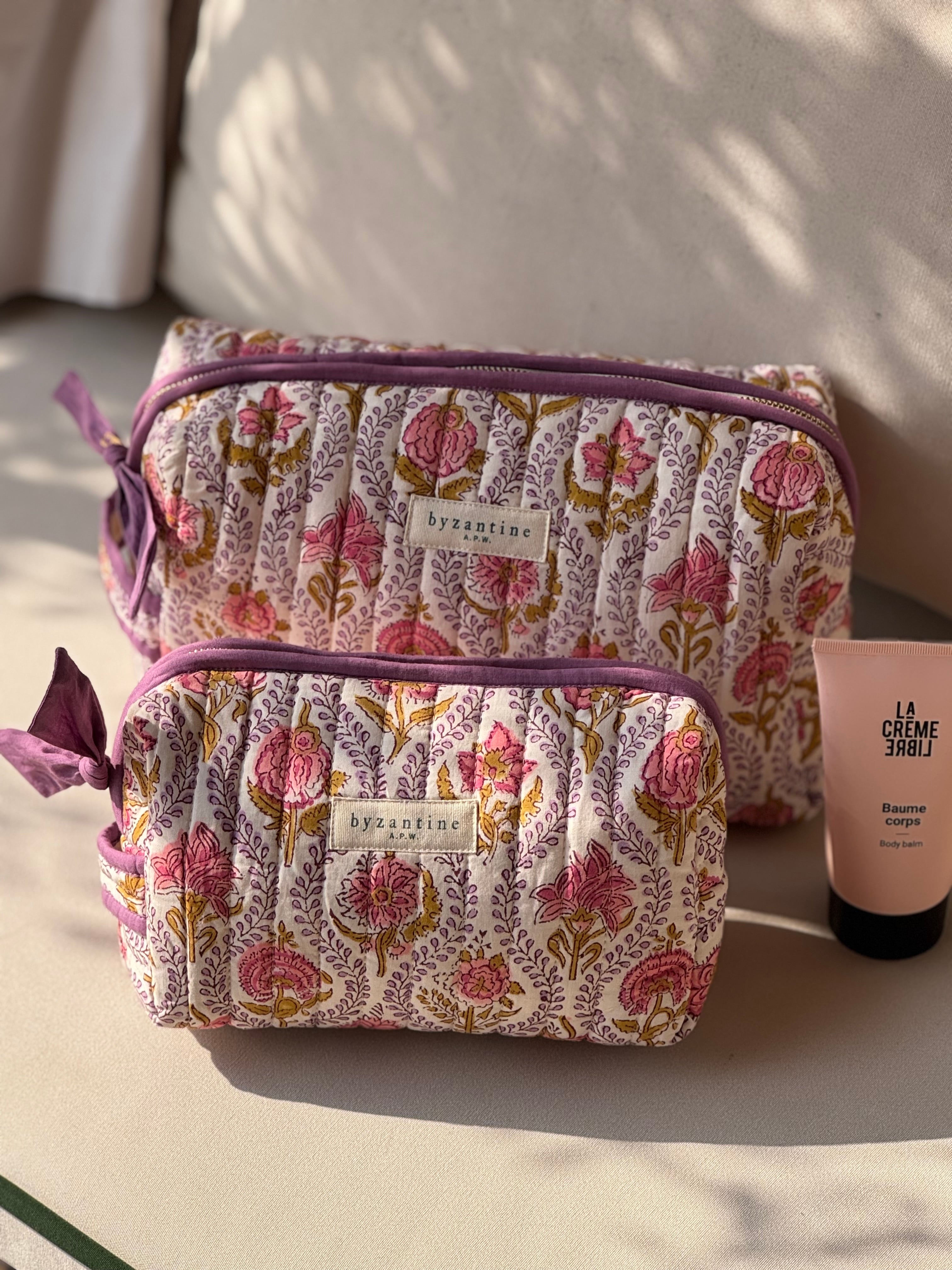 Duo de trousses de toilette Éphèse Rose sur un canapé, avec un tube de crème