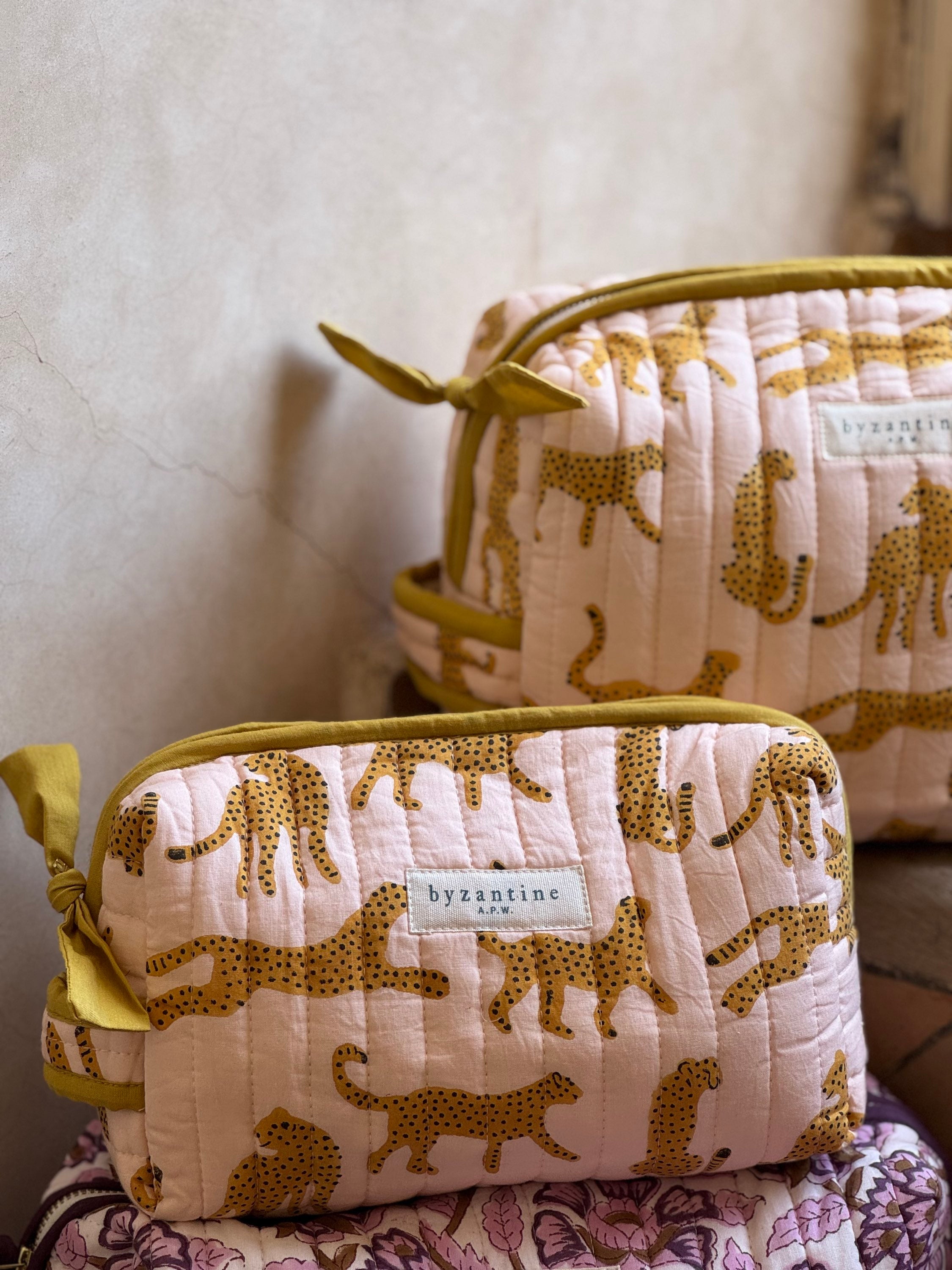 Trousses de toilette XL Fauve Rose empilées, étiquette Byzantine sur le coton matelassé