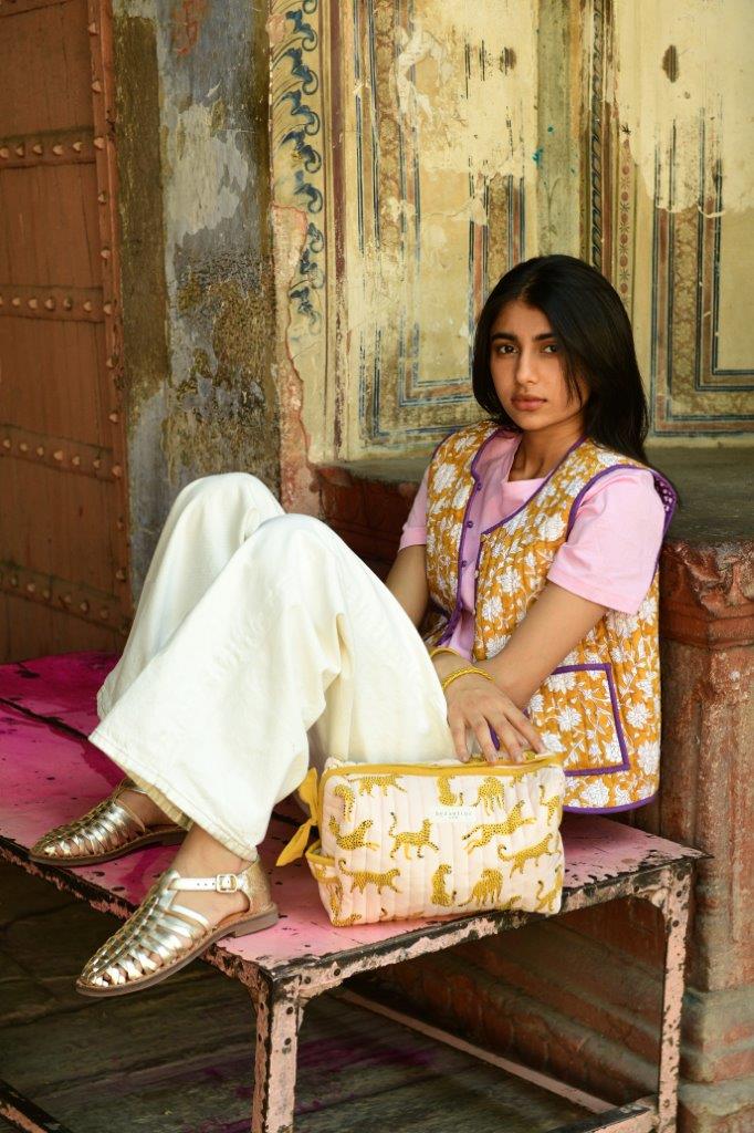 Femme assise sur un banc avec une trousse de toilette XL Fauve Rose à ses pieds