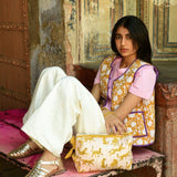 Femme assise sur un banc avec une trousse de toilette XL Fauve Rose à ses pieds