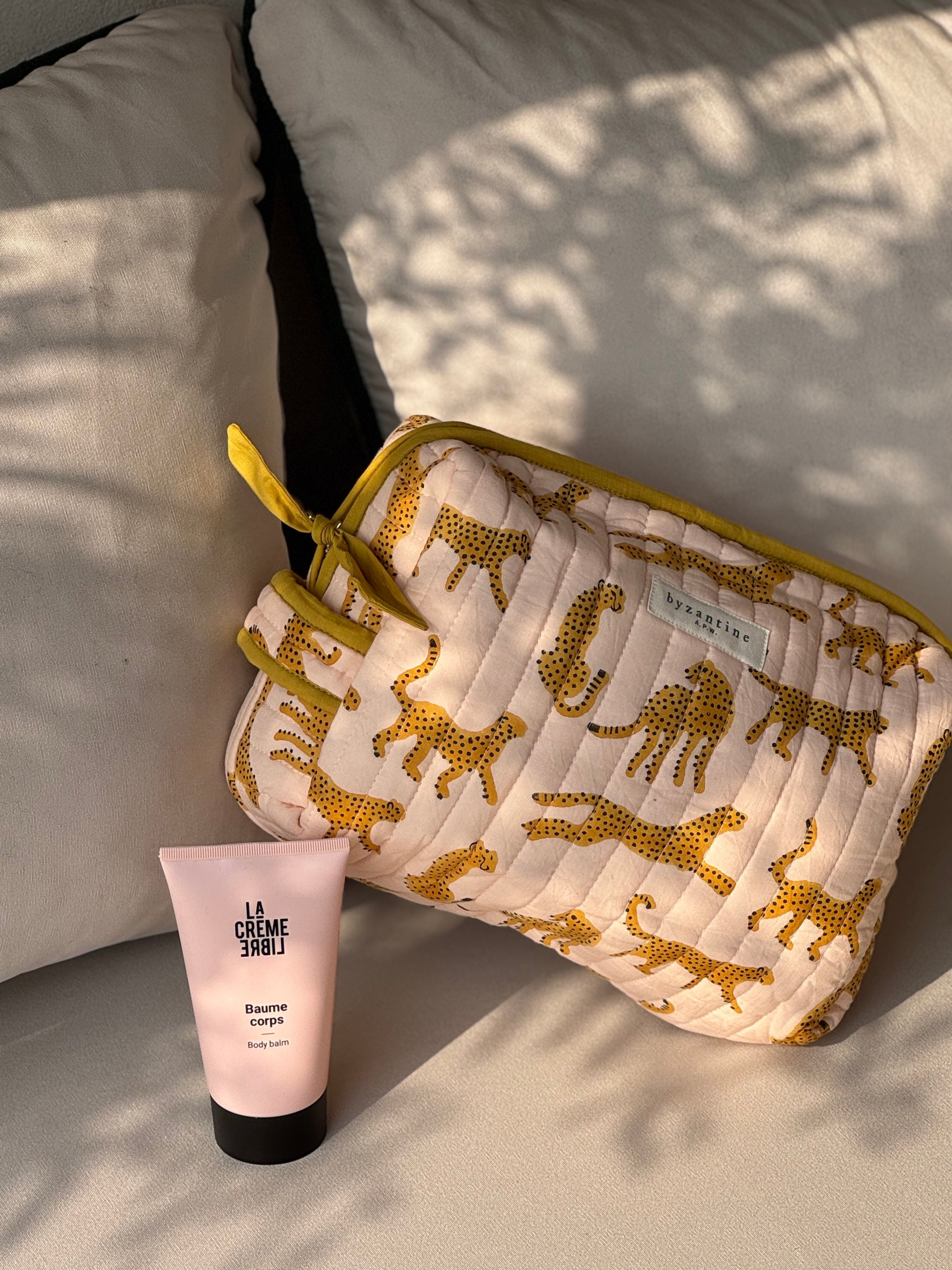 Trousse de toilette XL Fauve Rose de Byzantine avec un tube de crème, posée sur un coussin
