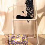 Trousse rabat N°113 Bleu au pied d'une chaise blanche, foulard bleu nuit sur le dossier