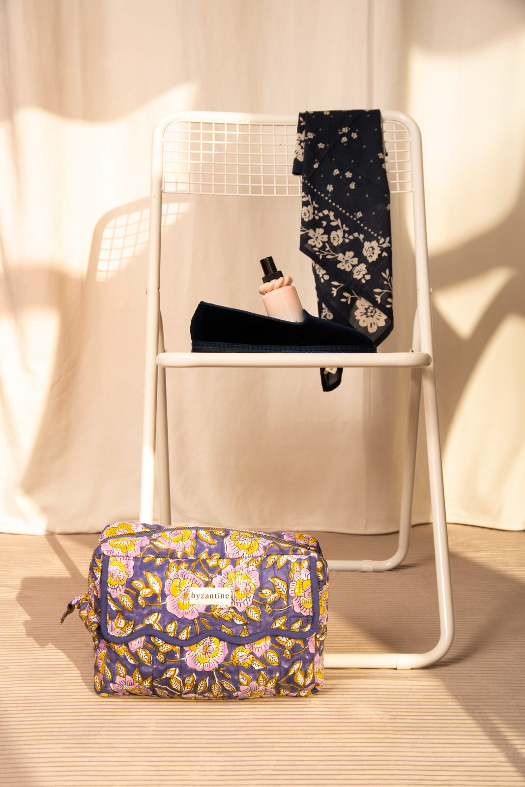 Trousse rabat N°113 Bleu au pied d'une chaise blanche, foulard bleu nuit sur le dossier