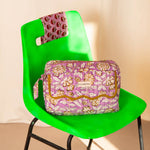 Trousse rabat Carthage Lilas à bord festonné moutarde, posée sur une chaise vert vif