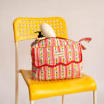 Trousse rabat Flora Rose à bord festonné rouge, rayures fleuries, sur une chaise jaune