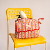 Trousse rabat Flora Rose à bord festonné rouge, rayures fleuries, sur une chaise jaune