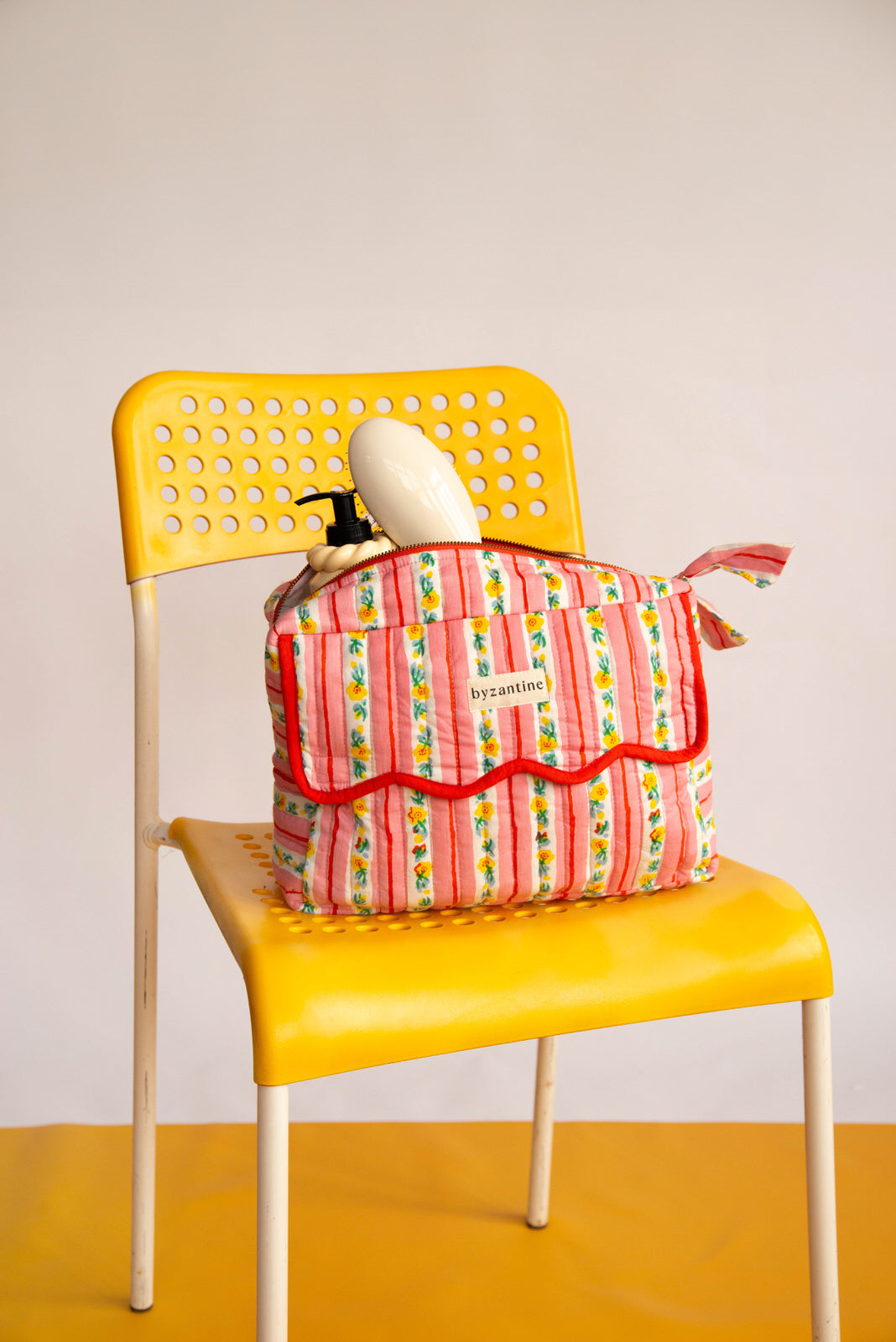 Trousse rabat Flora Rose à bord festonné rouge, rayures fleuries, sur une chaise jaune