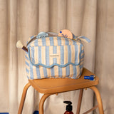 Trousse rabat Pacha Bleu ciel à bord festonné sur un escabeau en bois, savon à côté