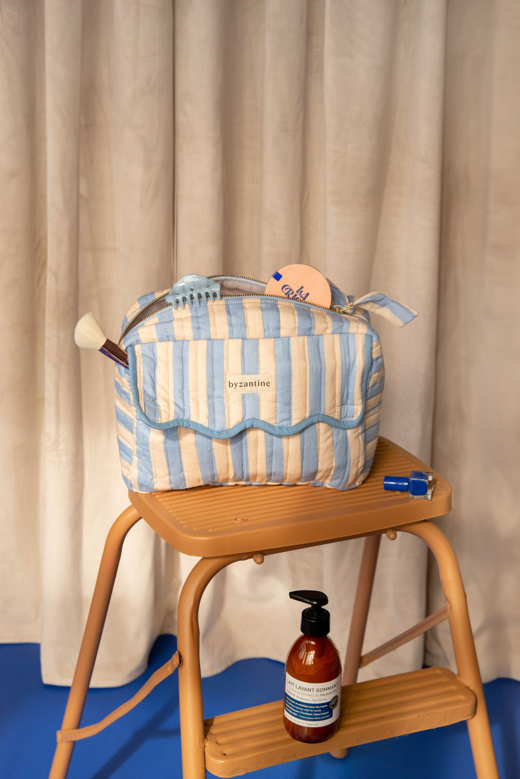 Trousse rabat Pacha Bleu ciel à bord festonné sur un escabeau en bois, savon à côté