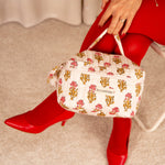 Trousse vanity N°50 Rose tenue par la poignée, escarpins et collants rouges